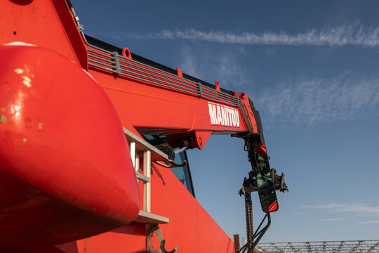 A red Manitou telehandler telescopic handler used for lifting materials on a construction site, showing the brand logo against a clear blue sky.