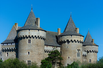 Obraz premium View of the medieval Castle of Suscinio under a clear blue sky, showcasing its stone walls, round towers, and reflective moat in the coastal landscape of Brittany.