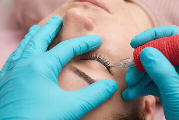 Permanent makeup artist applying eyeliner tattoo on woman's eyelid with precision in beauty salon