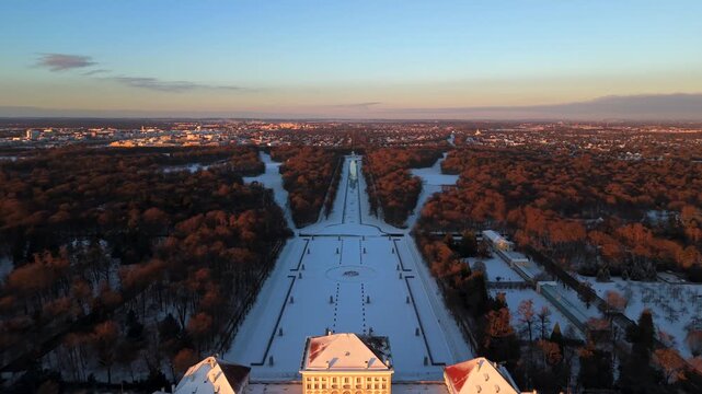 Panorama Luftaufnahme des Schlossparks Nymphenburg in Muenchen, Deutschland. Winterlicher Sonnenaufgang beleuchtet verschneite Parkanlagen, Kanaele und das barocke Schlossensemble