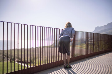 Naklejka premium Woman railing landscape view overlooking vineyard and sea on sunny hillside