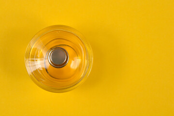 A high angle shot shows a round glass perfume bottle with a metallic cap placed on a bright yellow...
