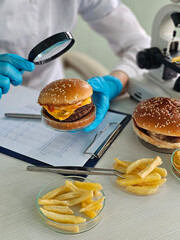 Scientist examines a hamburger and fries under a magnifying glass in a lab