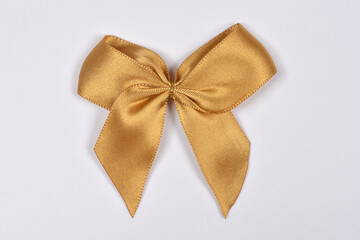 A top view of a single elegant golden satin ribbon bow centered on a plain white surface for decorative or gift packaging concepts