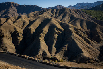 Dry mountain landscape with dramatic ridges and deep shadows, winding asphalt road in the foreground, arid highland terrain, natural patterns and textures, travel and nature background.