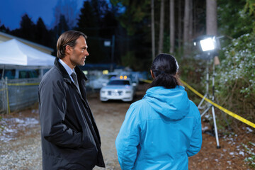 A male and female detective study evidence by their vehicle in the forest at night, depicting the focus required and the determination to seek justice in challenging conditions.