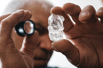 Mature goldsmith male inspecting uncut in raw diamond with magnifying glass