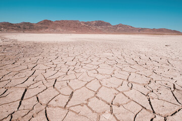 Cracked, dry desert land in the foreground with rocky mountains on the horizon under a clear blue sky. The concept of drought, climate change and extreme environmental conditions