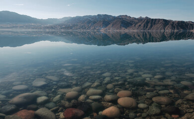 The Bartogai reservoir has crystal clear water reflecting the mountainous landscape of the Trans-Ili Alatau. Rocks at the bottom of the reservoir. The nature of Kazakhstan.