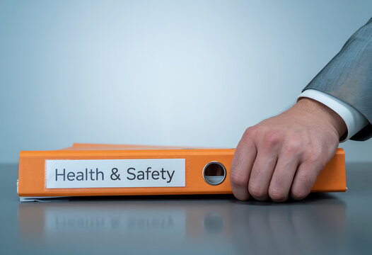 Professional Business Person Reaching for an Orange Health and Safety Compliance Binder