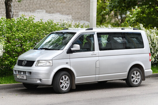 A silver Volkswagen Transporter minibus (pre-facelift T5, produced from 2003 to 2010) with a minivan body. The vehicle is parked parallel to the curb.