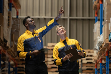 Two warehouse workers in safety uniforms coordinating inventory check with digital tablet and clipboard, showcasing teamwork, logistics planning, warehouse efficiency in industrial storage.