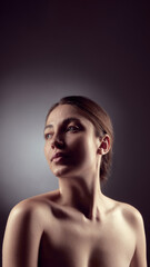 Fototapeta premium Low light studio portrait of young woman on dark background. Concept of natural beauty, skin tone realism, calm confidence, and minimalist visual language for beauty and wellness communication.