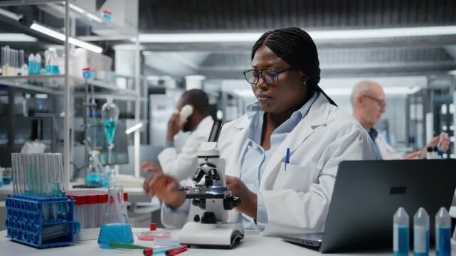 Clinical laboratory technologist pipetting blue liquid into test tube to analyze it. African american woman transferring chemical sample to prepare for immediate spectroscopic analysis, camera A