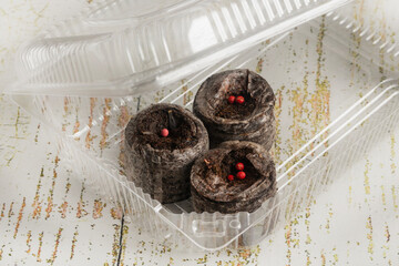 Three peat pellets with seeds, soaked in water, are placed in a plastic container that serves as a small greenhouse. Macro