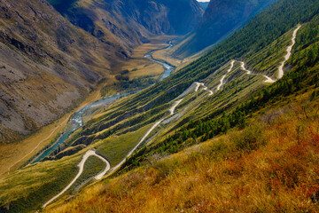 Winding mountain path with river valley and lush forest hills in summer Katu Yaryk pass Altay