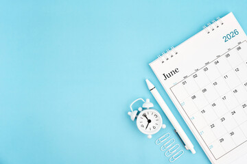 Fototapeta premium June 2026, Monthly desk calendar for 2026 year and alarm clock with paper clips on blue color background.