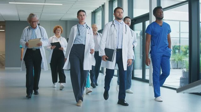 Confident medical team walking through clinic hallway preparing for upcoming operation. Focused doctors carrying tablets and reviewing tasks while moving together. Professionals showing determination.
