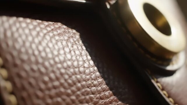 Extreme close-up of a round brass eyelet set into rich brown leather. The textured surface and visible stitching highlight craftsmanship.
