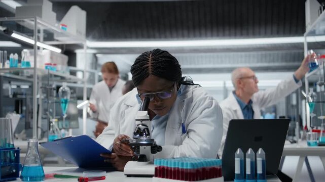 Female scientist using optical microscope to study microorganisms in laboratory, innovating. African american woman contributing to scientific community through detailed biological research, camera A