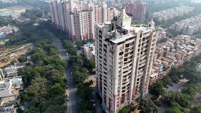 Wide aerial shot of Greater Noida cityscape in smoggy conditions, featuring planned commercial complexes, clustered housing, tree-lined areas, and elevated roads, reflecting a fast-developing NCR hub.