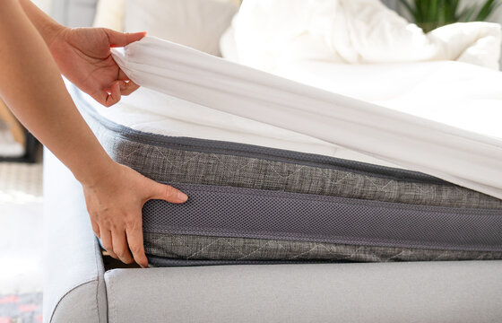 Changing bed sheets. Woman is putting on a fitted white cotton sheet on a mattress while making the bed. 