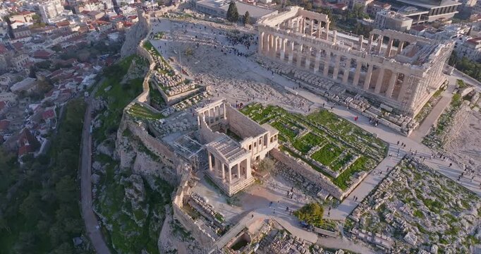 Cinematic drone flight from the Erechtheion toward the Parthenon on the Acropolis in Athens, Greece. Tourists walking among ancient ruins create a lively historic scene ideal for travel and culture.
