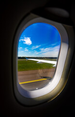 Airplane window view of runway and green field.