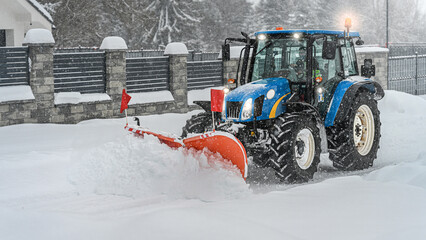Tractor with a snow plow clear snow from the road after blizzard. Winter road maintenance.
