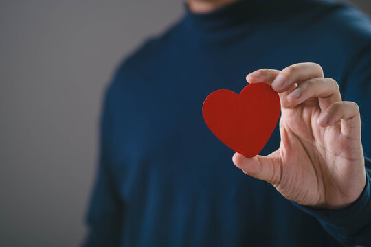 Hand holding red heart symbol, representing love, care, compassion, trust, emotional connection, charity, healthcare support, customer loyalty, and human values concept on minimal background.