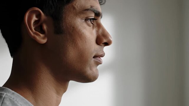 Profile view of a young south asian man looking pensive and thoughtful, closing his eyes in a moment of quiet contemplation and reflection, finding peace and tranquility indoors