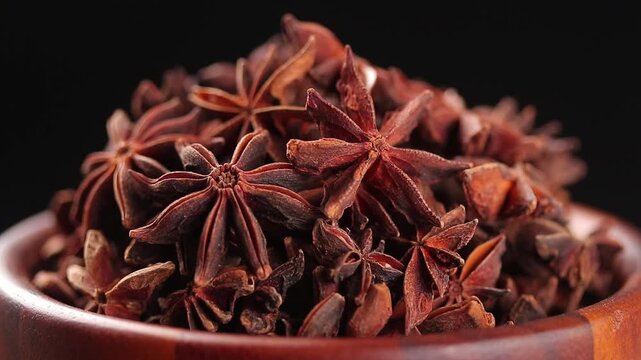 Pile of star anise in a brown wooden bowl rotating slowly on a black background.