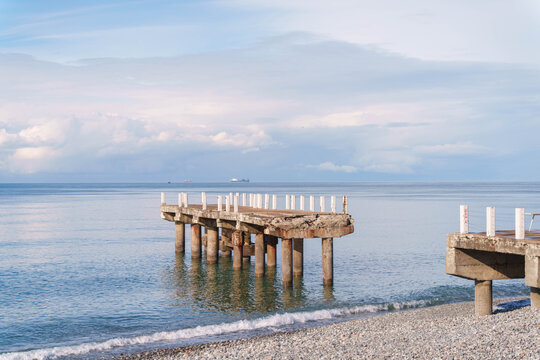 Damaged pier stretching into sea with ships on the horizon