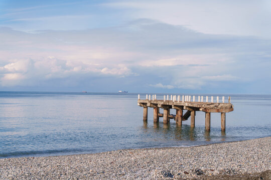 Damaged pier stretching into sea with ships on the horizon