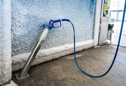 Winter weather damage: high-pressure washing nozzle and hose encased in thick ice at an outdoor, self-service car wash
