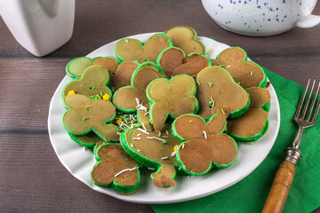 Shamrock shaped green tasty sweet pancakes for St Patricks day breakfast. Creative homemade tasty fried pan cakes with sugar sprinkles and Saint Patrick holiday decor