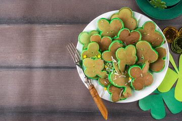 Shamrock shaped green tasty sweet pancakes for St Patricks day breakfast. Creative homemade tasty fried pan cakes with sugar sprinkles and Saint Patrick holiday decor
