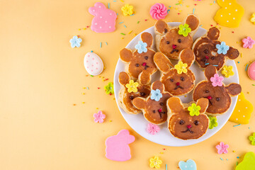 Cute and sweet Easter breakfast pancakes in form of bunny rabbits with sugar sprinkles flowers, rabbits on light yellow background