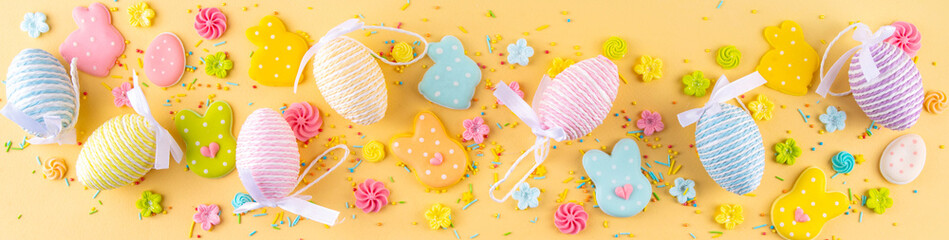 Cute and bright pastel colored Easter eggs and bunny background. Pink. blue, yellow colored bunny rabbits, eggs and flowers sugar sprinkles on light yellow background