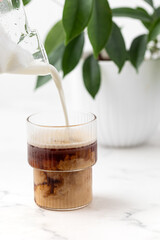 adding frothed milk to a glass of coffee, iced latte