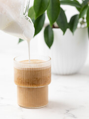 adding frothed milk to a glass of coffee, iced latte