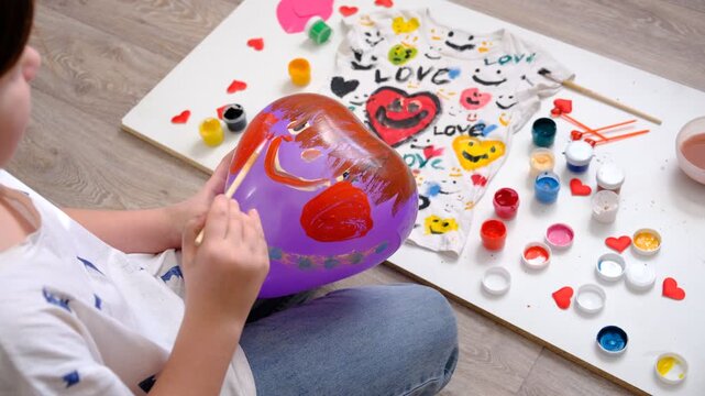 Teenager girl sitting on the floor and painting coloring white t shirt and balloon, funny face. Creative. Gift for Mothers day, Fathers day, Birthday, Valentines day. Kid craft. Home education game. 