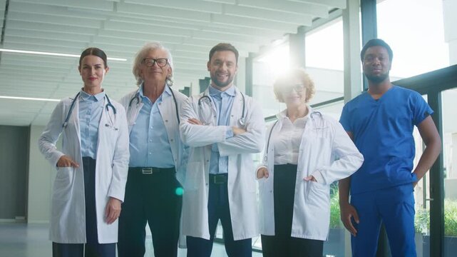 Medical team posing proudly in bright hospital corridor. Standing with confident expressions. Showing teamwork spirit and presenting strong professional image during active clinical routine.