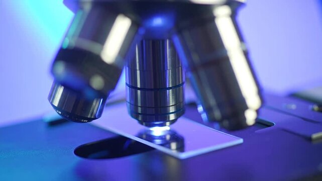 Close-up of a scientific microscope with a slide in view, bathed in cool blue light