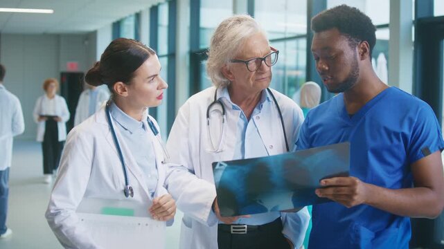 Medical team reviewing chest X-ray together in bright corridor. Nurse seeking clarification while two experienced doctors explain findings. Collaborative discussion focused on patient diagnosis.