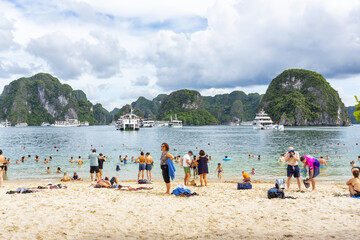 Obraz premium Sandy beach crowded with tourists, overlooking the cruise ships and limestone karsts of Ha Long Bay