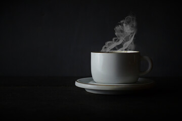 A cup of hot coffee with steam on a dark background.