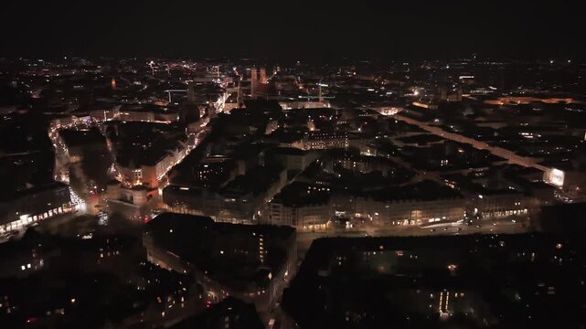 Drohnenvideo von Muenchen bei Nacht. Blick ueber die Isar auf die hell leuchtende St. Lukas Kirche and die fernen Wahrzeichen der Stadt wie die Frauenkirche und das Neue Rathaus am Marienplatz.