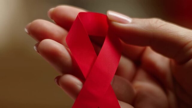 Detailed View Of Female Hands Clutching Red Ribbon Representing Support And Unity Against HIV