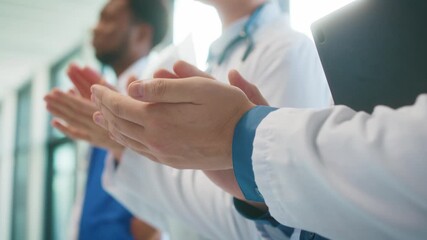 Close view of doctors clapping in bright hospital corridor. Holding tablet while joining applause. Celebrating teamwork and acknowledging effort during busy clinical routine. Sunlight in background.